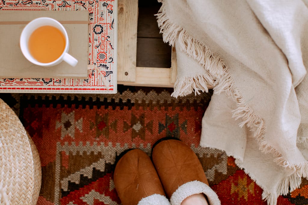 A pair of feet in cozy slippers next to a cup of tea and a blanket