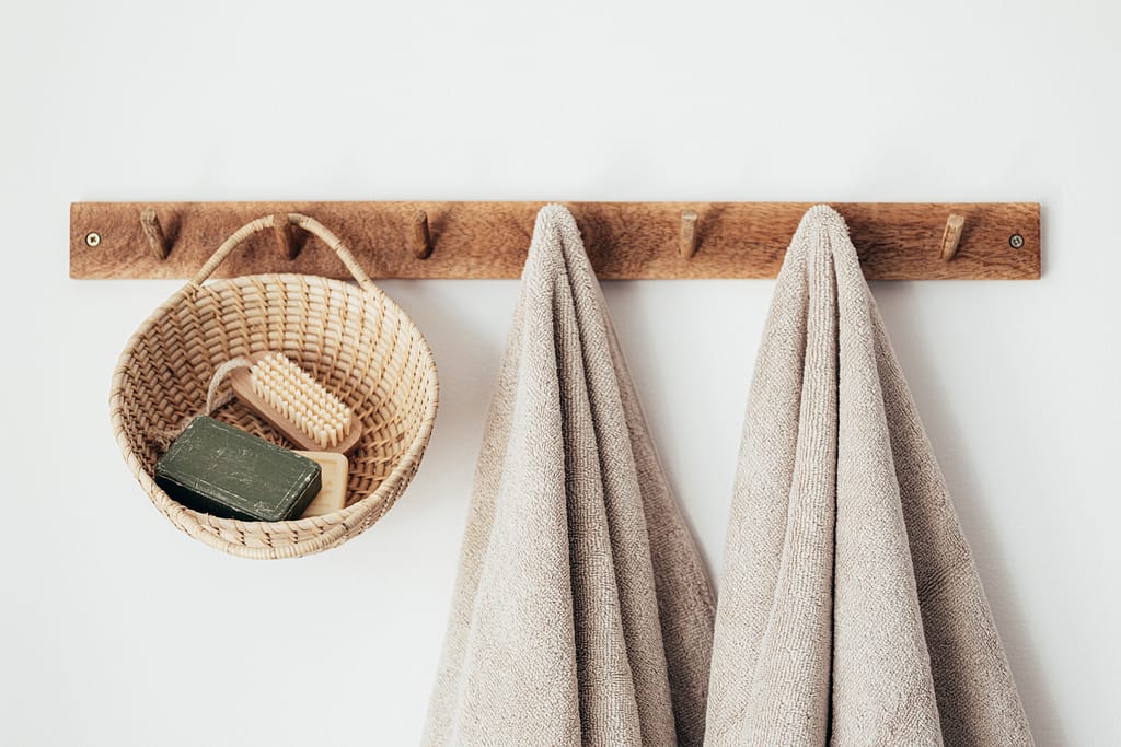 A wooden towel hook with two towels hanging on it and a wicker basket