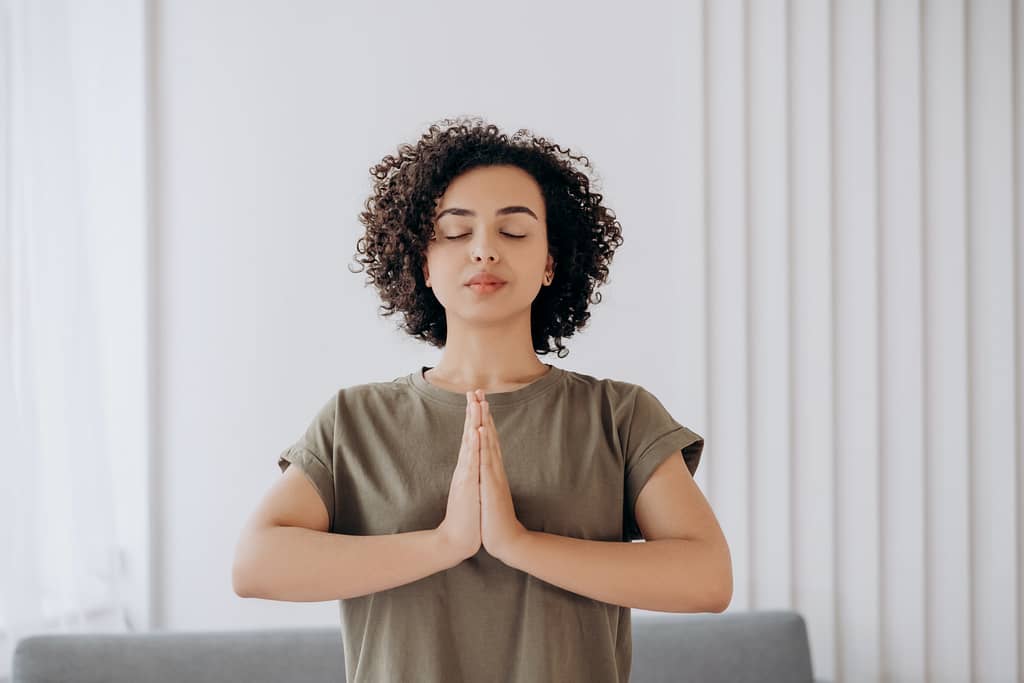 A woman standing with her eyes closed and hands in prayer position