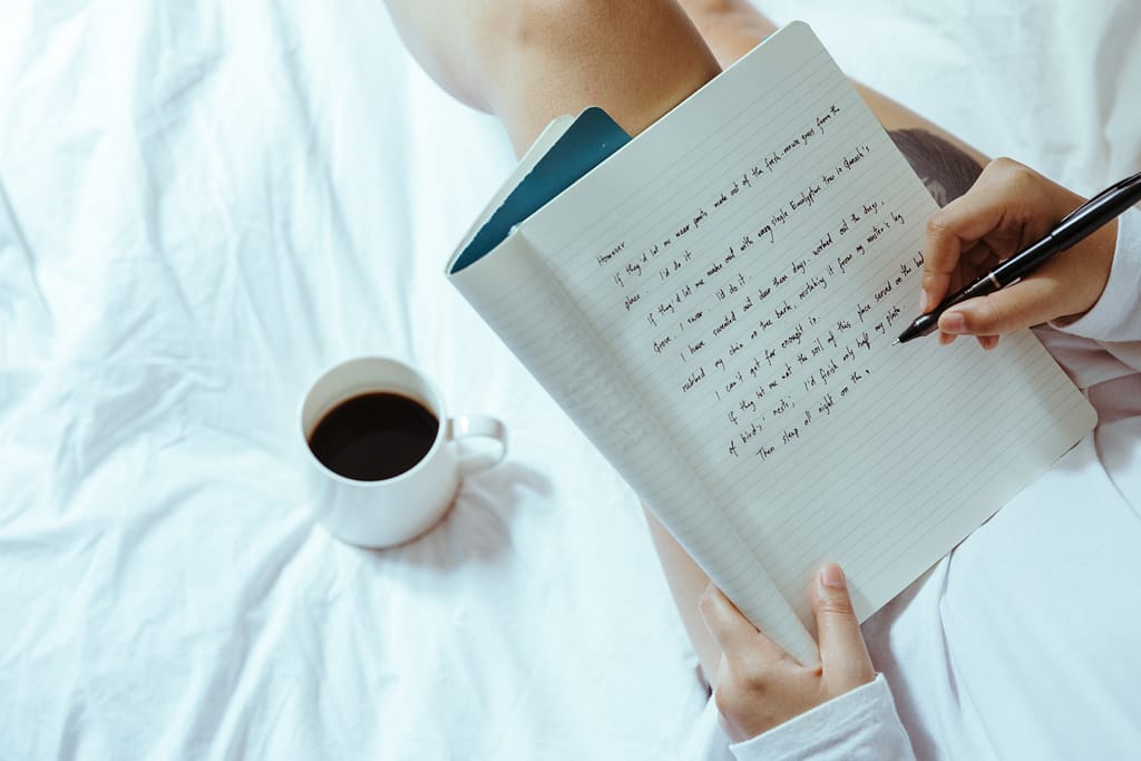 A person journaling on their bed with a cup of coffee beside them