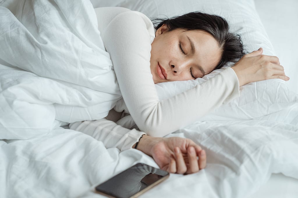 A woman sleeping in bed wih her phone next to her