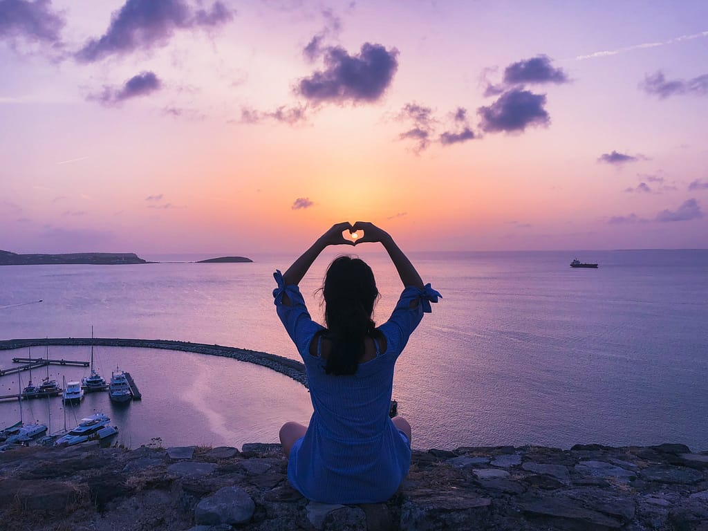 A woman sitting on a rock doing a heart shape gesture with her fingers