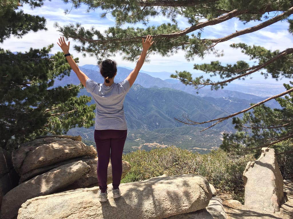 Getaway House Big Bear Pantea Rahimian looking away with her hands up while hiking at Kellers Peak