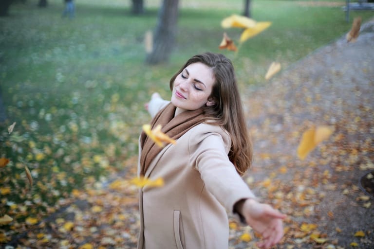 Woman with open arms while leaves are falling