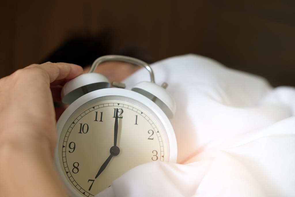 Person holding a large alarm clock in bed