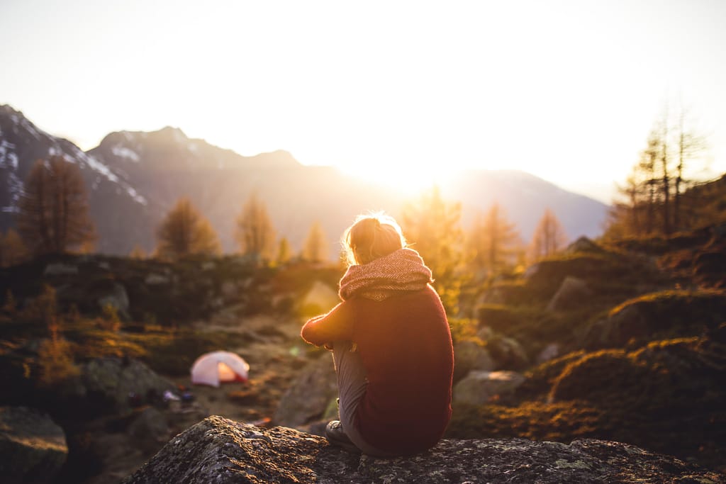 A person sitting and looking at a mountain and sunset
