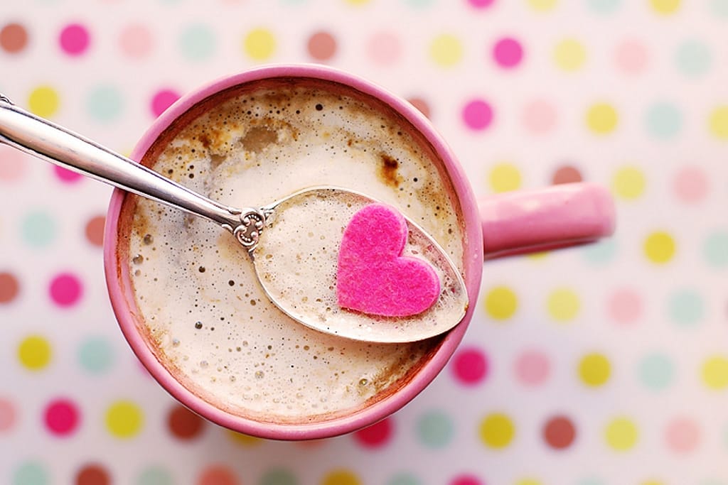 A cup of hot coco with a spoon and a heart shaped cookie