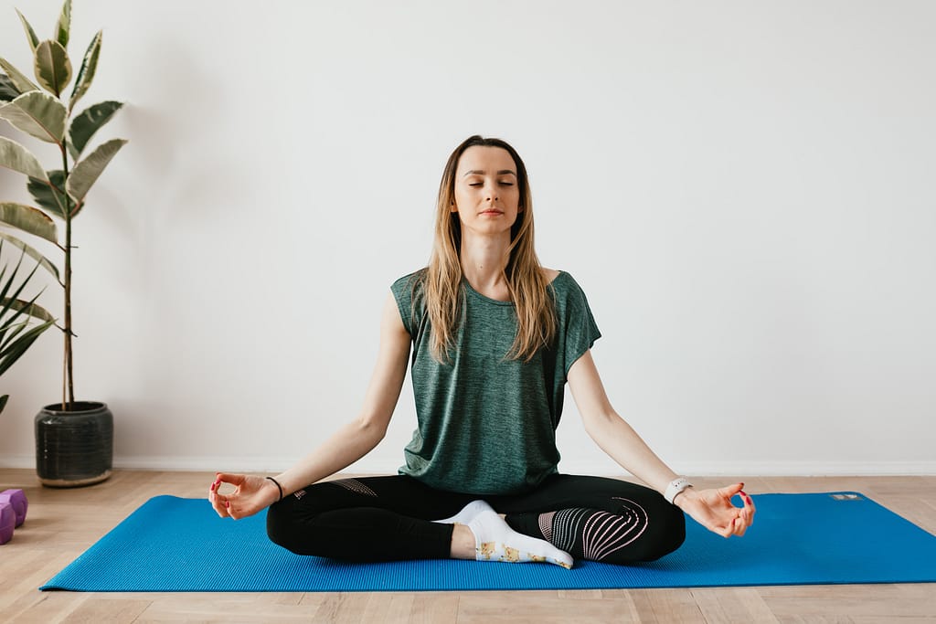 A woman meditating with her legs crossed on a yoga mat