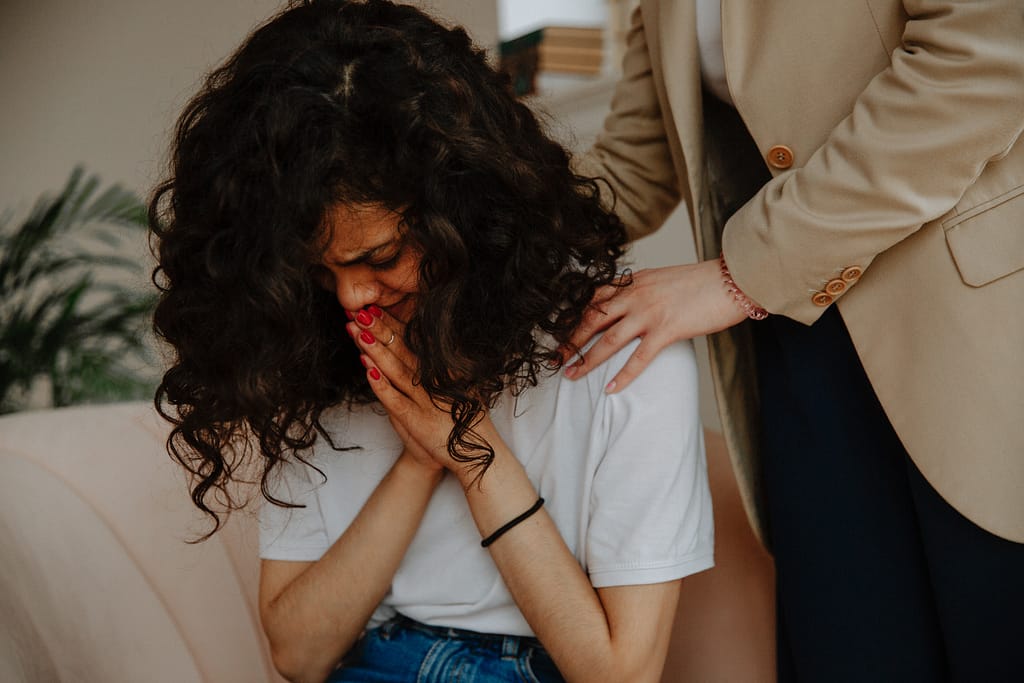 A woman crying while her therapist is touching her shoulder