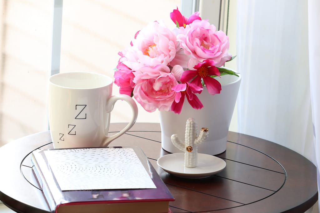 A mug next to a vase with roses and a notebook
