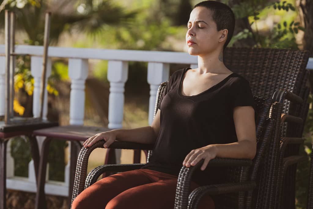 A woman meditating with her eyes closed on a chair outside on a deck