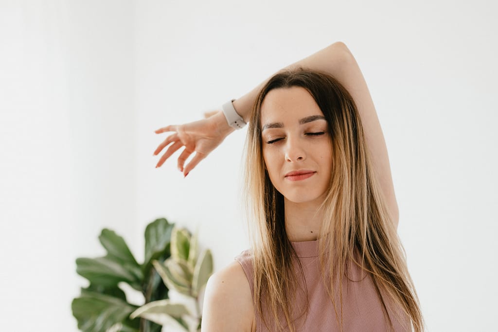 A woman with her eyes closed stretching her arm around her head to practice self-care