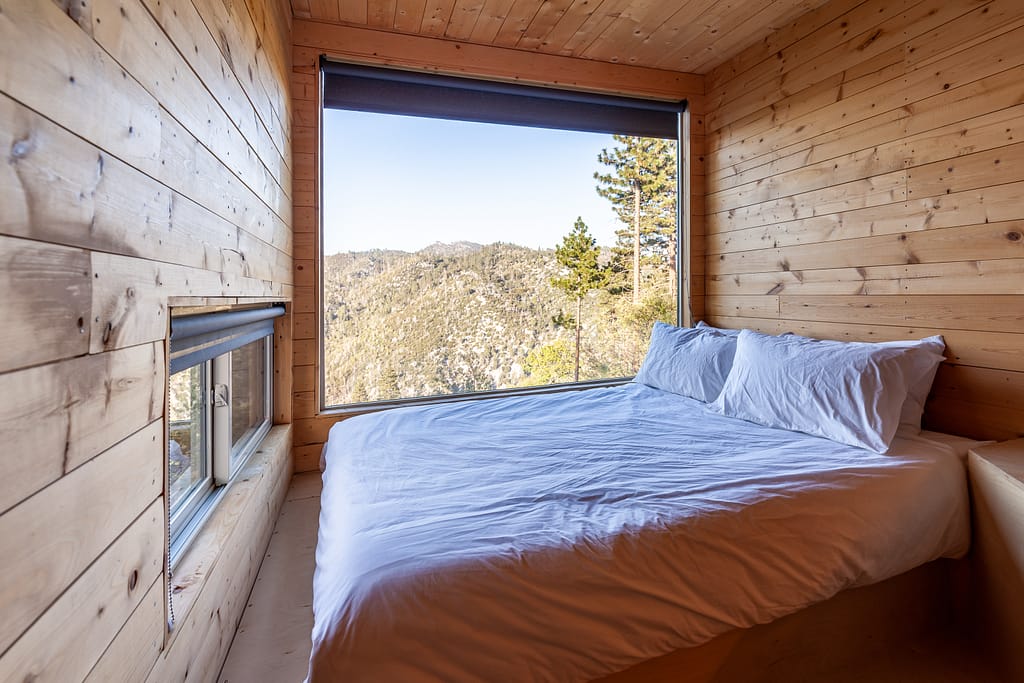 Getaway House Big Bear interior of cabin with bed and huge window overlooking valley