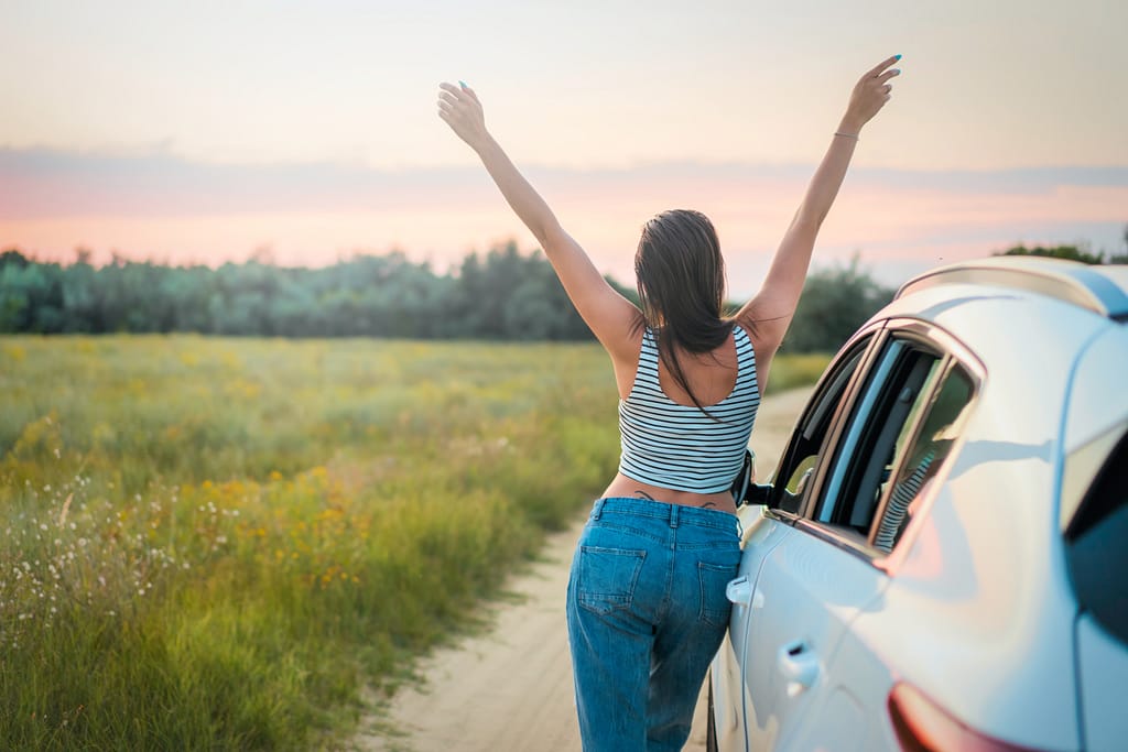 How to beat anxiety: a woman with her back standing next to a car and her arms in a V