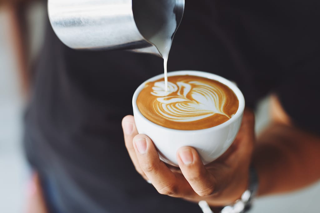 A barista pouring milk into a cup of coffee